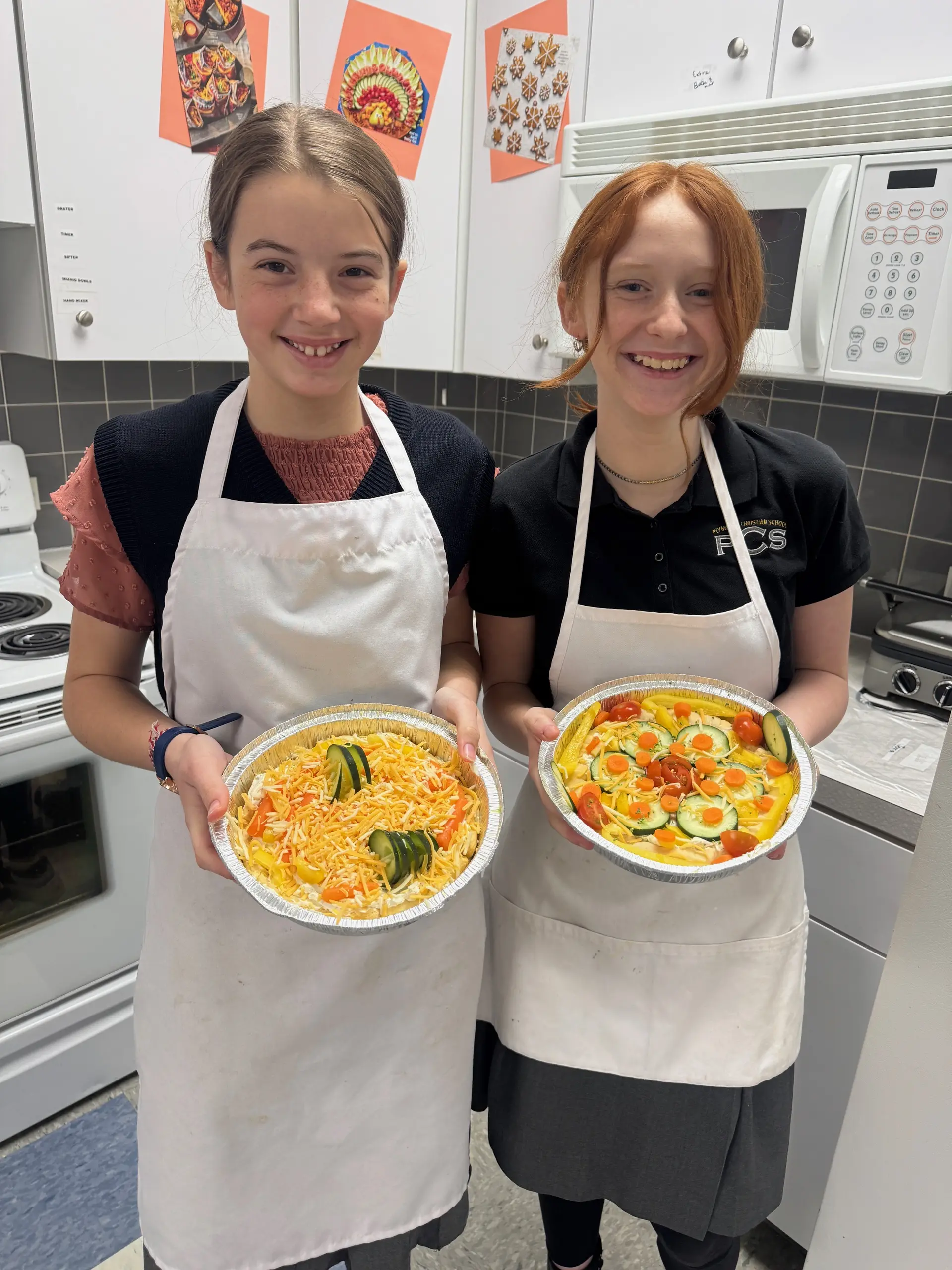 Two students in aprons holding the pizzas they made