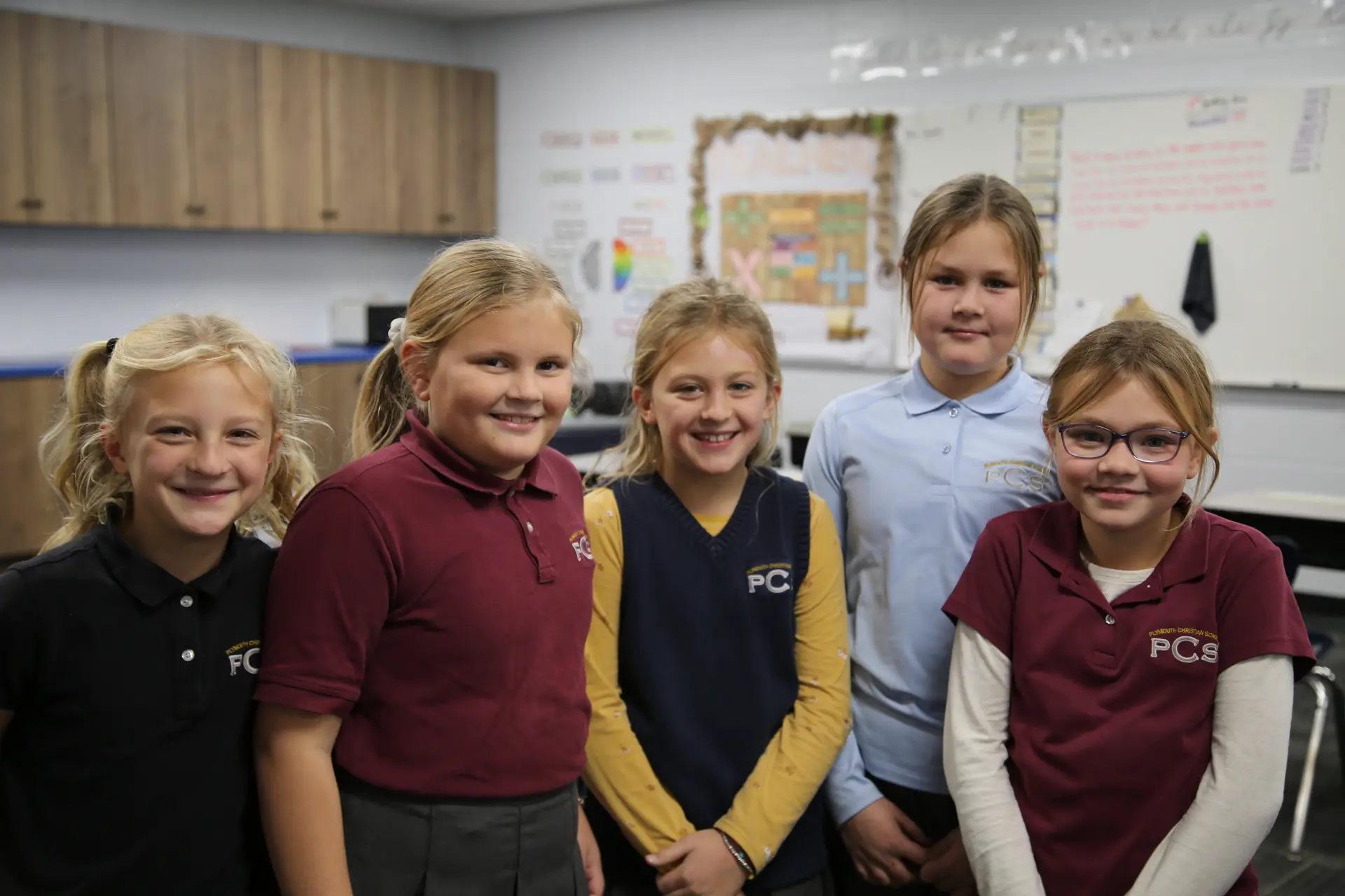 Five smiling students posing together in their classroom