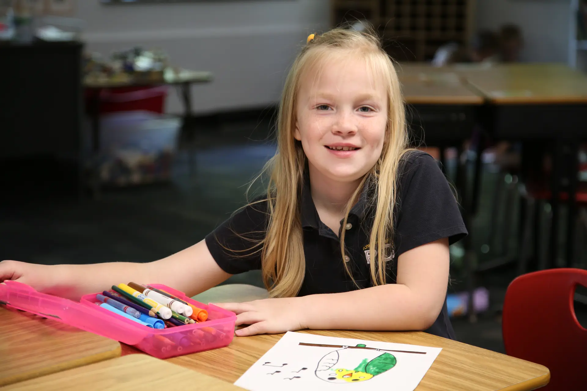 A smiling student drawing with markers at her desk