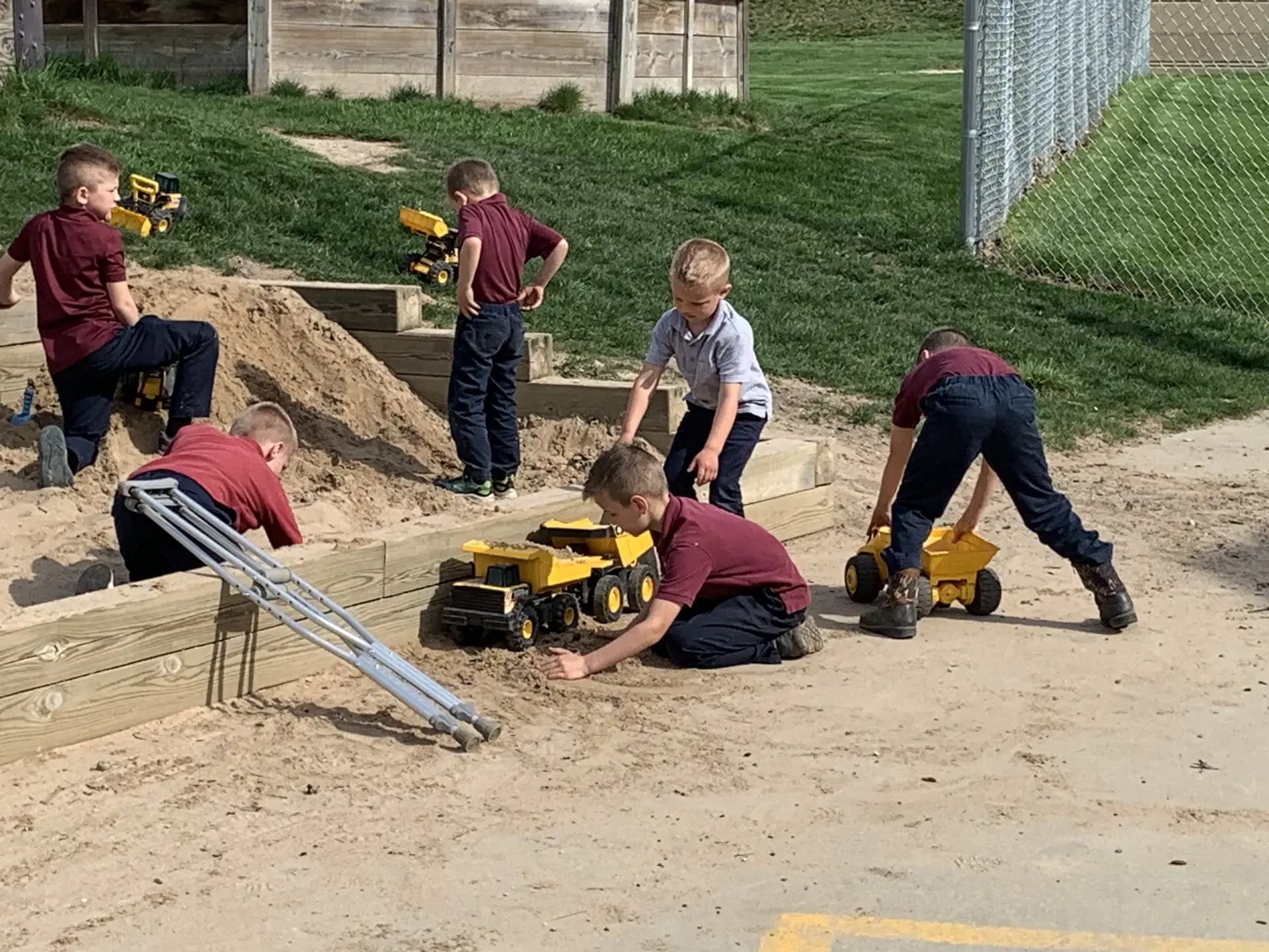 Students digging with toy trucks in the school sandbox